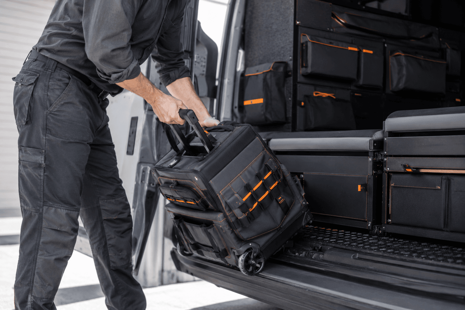 A tradesperson loading an unbranded rolling case into an organised cargo van
